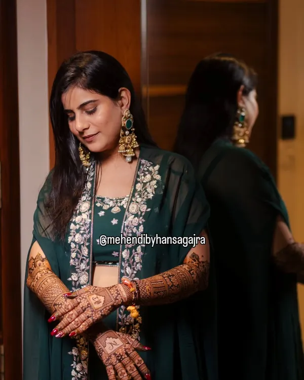 A quiet moment of reflection for the bride, admiring her intricate mehendi. Her elegant green outfit and the warm lighting make this a truly beautiful and emotional shot.