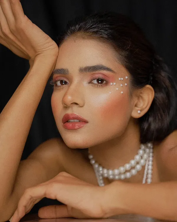 A stunning beauty portrait featuring a model with delicate pearl accents around her eye. The soft lighting and close crop emphasize the flawless makeup and the elegance of the pearl theme.