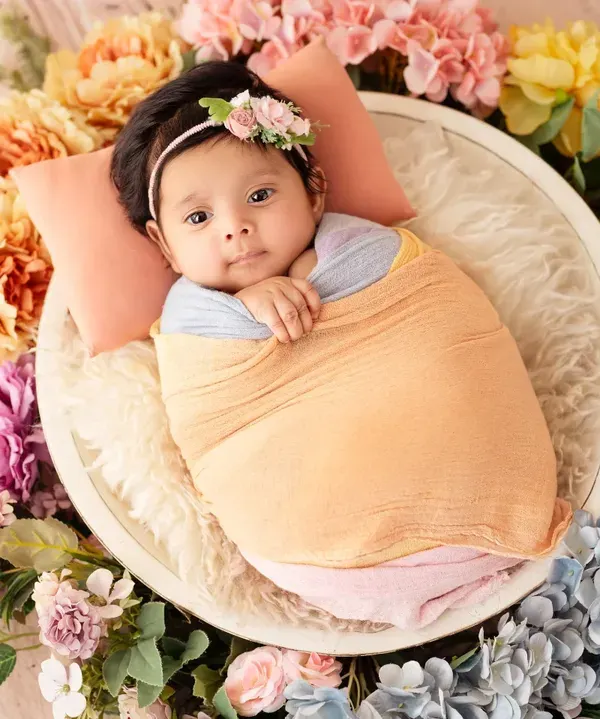 An awake and alert baby girl, wrapped in pastel colors and lying in a bowl surrounded by a beautiful ring of flowers.