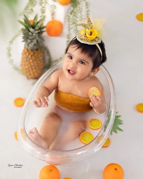 A happy splash! This baby girl is loving her 9-month milestone fruit bath session, surrounded by cheerful oranges and pineapple props.