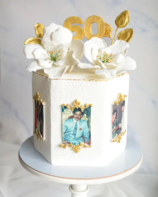 Celebrating 60 years in style with this elegant hexagonal cake. It features edible photos in gold frames and is topped with beautiful, handmade white sugar flowers and a gold "60" topper.