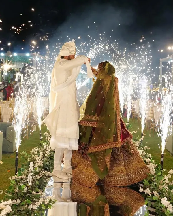 A stunning Varmala moment on a raised mirror stage. The couple is surrounded by an arc of cold pyro fountains, with their reflection creating a beautiful and complete picture.
