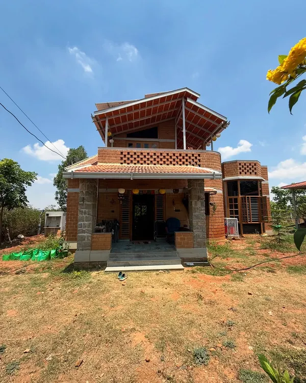 A full view of our completed eco-friendly farmhouse project. The design incorporates a multi-level roof and a welcoming porch with stone pillars, showcasing a blend of traditional and sustainable architecture.