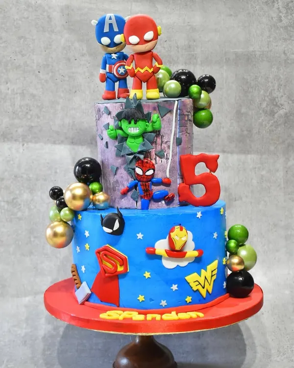 A superhero spectacular for a 5th birthday. This three-tier cake brings together the Avengers and DC heroes with edible figurines of Captain America, Flash, Hulk, Spider-Man, and more, all made with a delicious chocolate hazelnut flavor inside.
