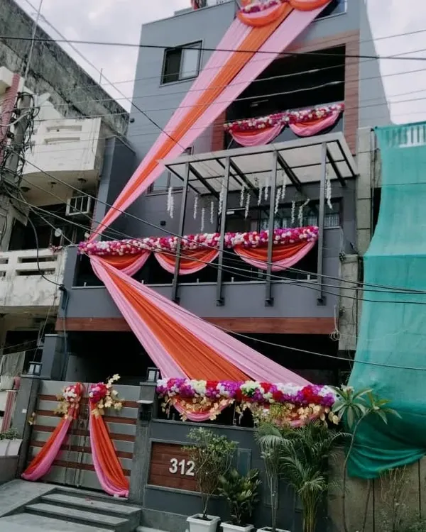 Another example of a full house front decoration for a wedding. I used long, flowing drapes in pink and orange, along with floral garlands on the balconies and gate, to give the home a festive look.