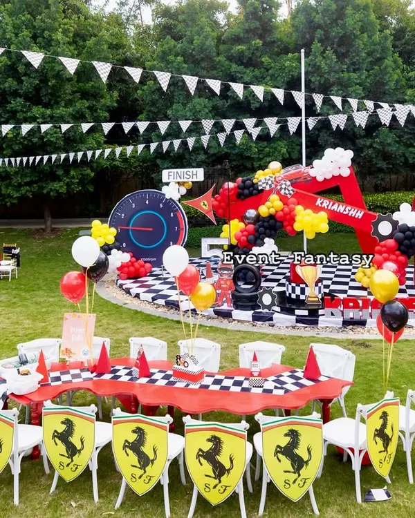 A fantastic outdoor Ferrari-themed party for Krianshh. This wide shot shows the main stage, the kids' dining area with custom chairs, and the expansive lawn perfect for racing games.
