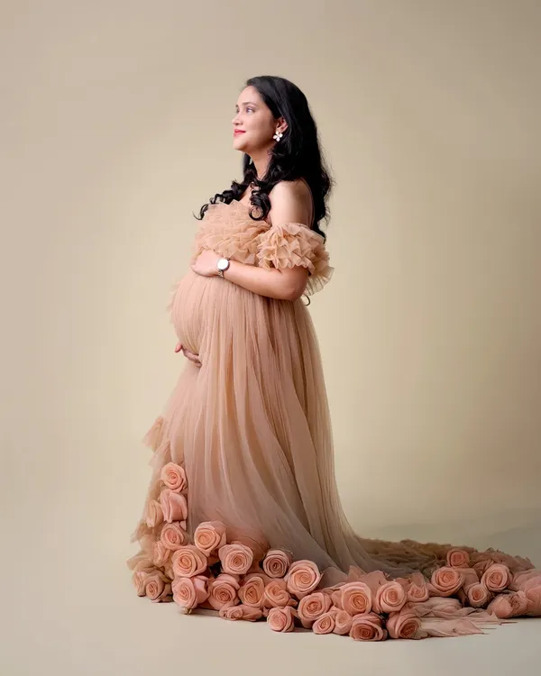 This unique maternity gown features a trail of delicate fabric roses, creating a stunning and romantic effect. It's one of the many designer options available in our studio wardrobe.