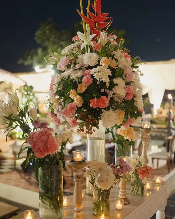 A lush and romantic floral centerpiece, combining roses, lilies, and chrysanthemums in shades of pink and white. I use abundant, high-quality florals to create a feeling of opulence and luxury.