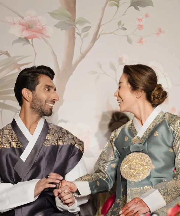 A beautiful, intimate moment between the Indian groom and Korean bride during their Paebaek ceremony. Dressed in traditional Hanbok, they share a smile against a delicate floral backdrop I designed for them.