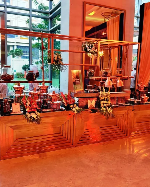 A wide view of our elegant buffet and live station setup for a corporate event. The wooden counters and floral arrangements create a warm and inviting atmosphere for guests.