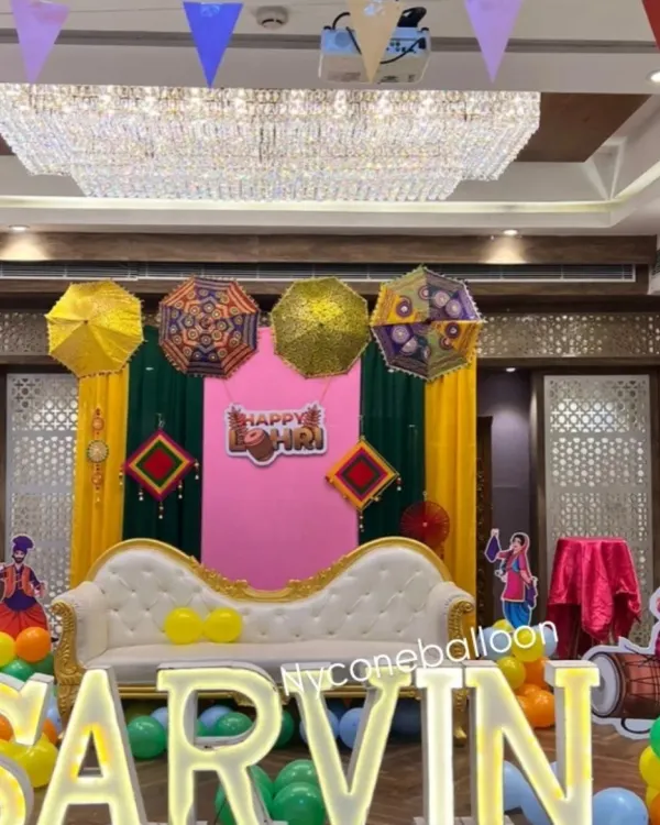 For baby Sarvin's first Lohri, I created this personalized stage featuring large, illuminated letters of his name. The setup includes a comfortable sofa for the family, colorful drapes, and festive Punjabi elements like decorative umbrellas.