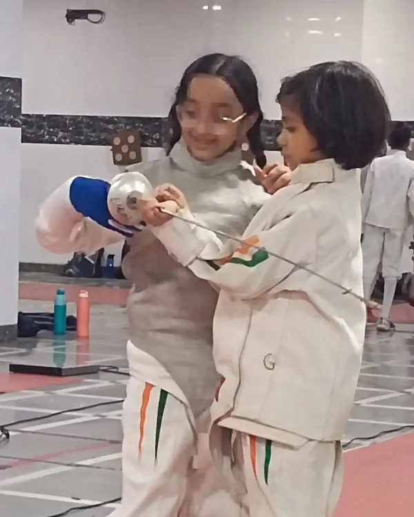 This is what our community is all about. A senior fencer takes the time to guide a younger member, adjusting her grip and sharing valuable experience.