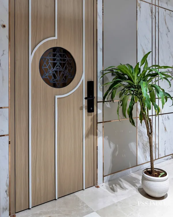 Sometimes, simple is better. This modern entryway is defined by its clean lines, with a statement wooden door featuring a geometric grill, a marble-paneled wall, and a single plant for a touch of life.