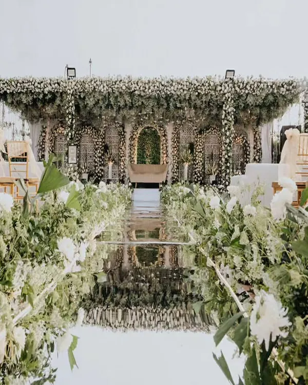 This is where dreams take shape. We designed this breathtaking engagement setting with a mirrored aisle reflecting an abundance of white florals and lush greenery, creating an ethereal walkway for the couple's grand entrance.