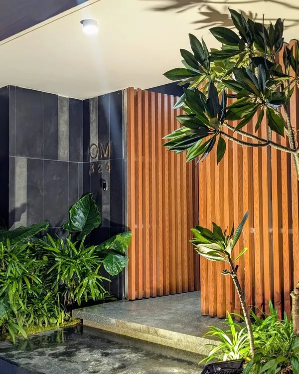 A modern home entrance featuring a striking combination of wood slats, dark tiles, and lush greenery. A small water channel and strategic lighting create a sophisticated and welcoming first impression.