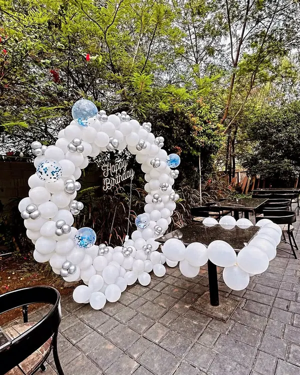 An elegant adult birthday party setup in a garden, featuring a white and silver balloon ring that doubles as a photo booth.