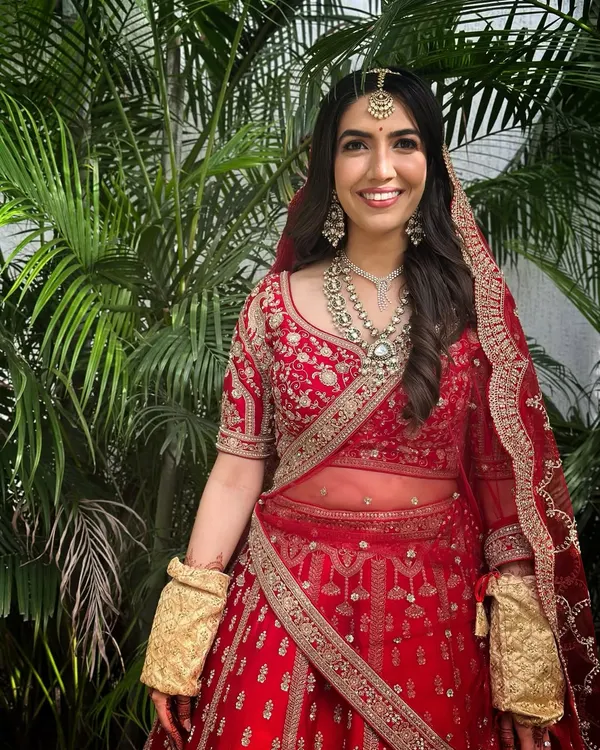 A classic North Indian bridal look. Draped in a magnificent red lehenga, her makeup is radiant and glowing, with defined eyes and a soft lip, letting her joyful smile be the focus.