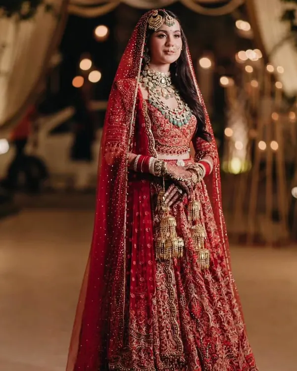 A breathtaking full-length shot of the bride in a classic red Tarun Tahiliani lehenga. The intricate embroidery and timeless silhouette make this a truly iconic bridal look.