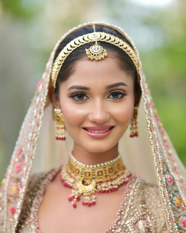 A perfect example of a soft and glowy pastel bride. The makeup is minimal yet impactful, with a focus on luminous skin, soft eyes, and a natural pink lip to complement her beautiful pastel and gold lehenga.