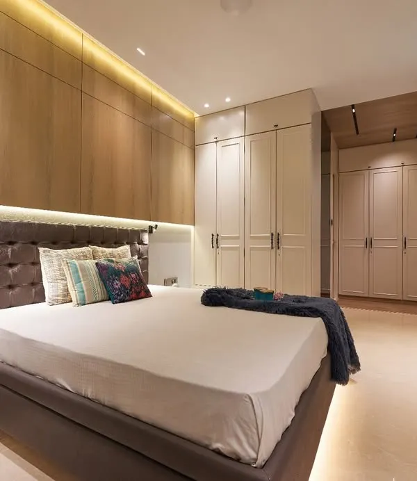 This master bedroom combines warm wood paneling on the feature wall with sleek, off-white wardrobes. We used integrated LED strip lighting above the headboard and below the bed to create a soft, ambient glow and a floating effect.