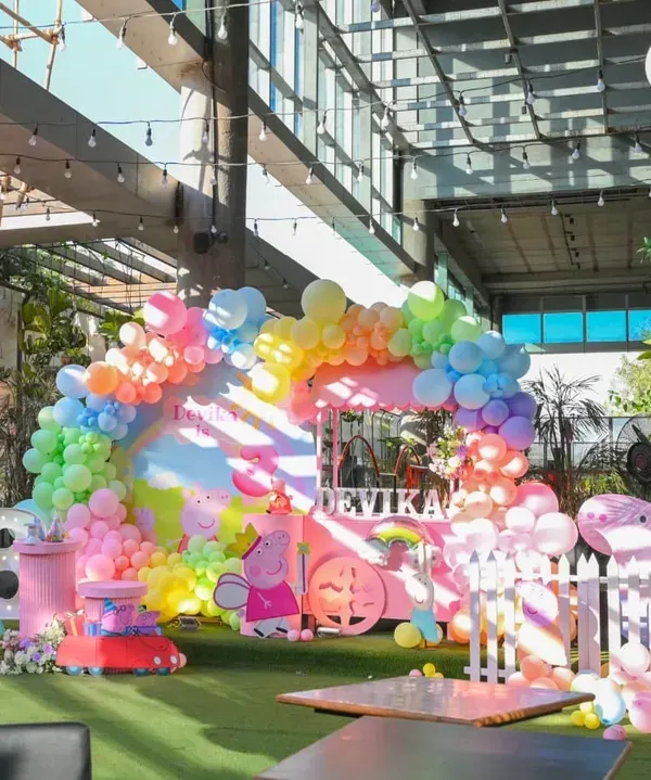 A full view of the vibrant Peppa Pig themed party, showcasing the colorful balloon arch, character props, and a custom dessert cart, all set up in a bright, open venue.