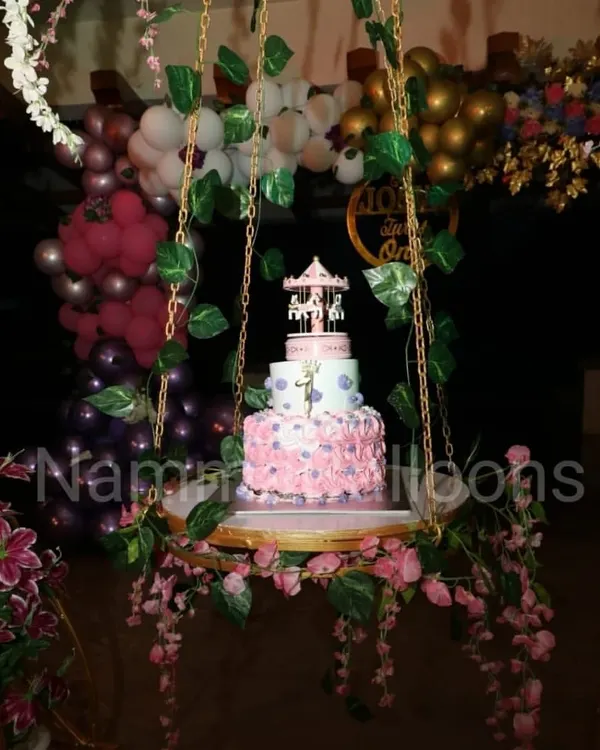 A unique cake display can be a centerpiece of the party. Here, a beautiful birthday cake is presented on a swing decorated with flowers and vines, adding a touch of magic to the celebration.