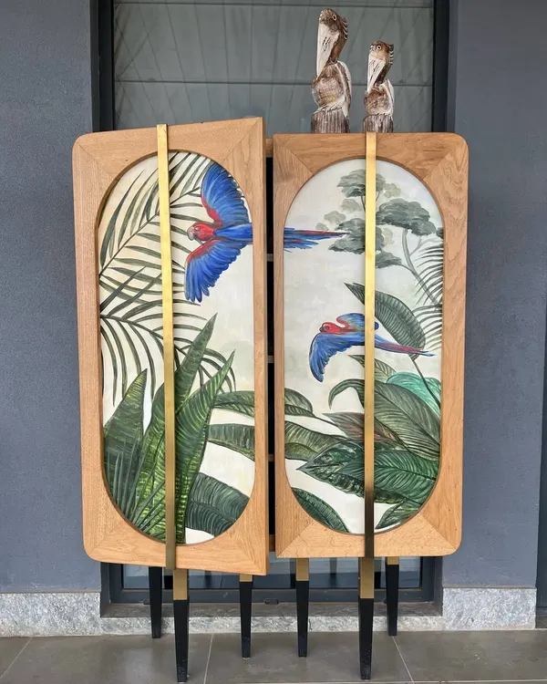 This hand-painted bar cabinet brings a touch of the tropics indoors. The vibrant artwork is balanced by the natural oak frame and minimalist brass hardware, creating a piece that is both a functional bar and a work of art.