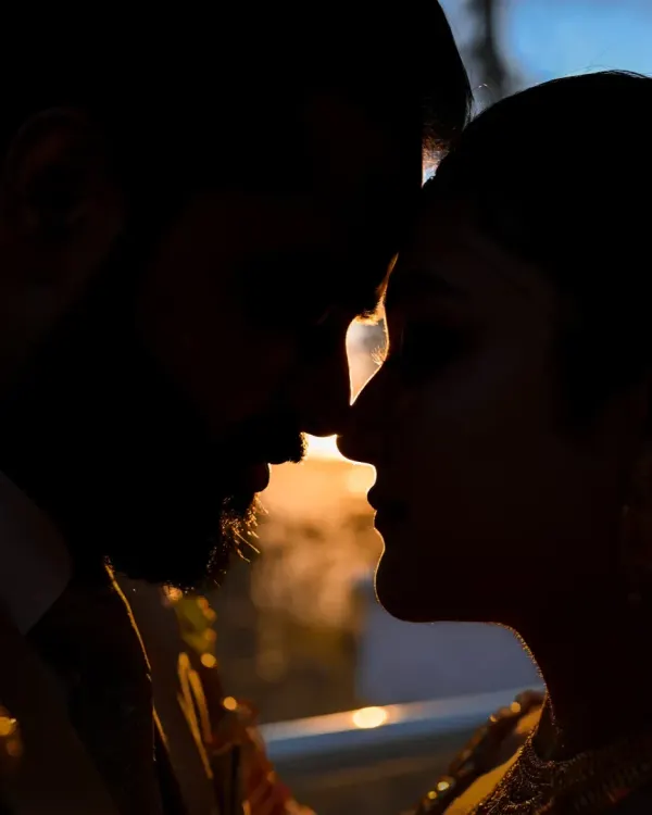 A powerful close-up silhouette of the couple, their faces close together, with the last light of the sun creating a fiery rim light around them.