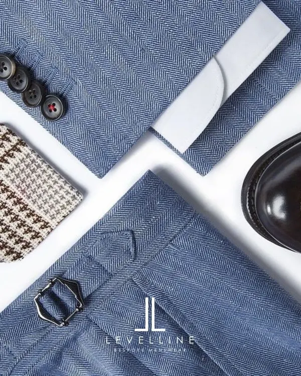 A flat lay showcasing the key elements of a bespoke outfit: herringbone fabric, side adjusters on the trousers, classic buttons, and a complementary pocket square.