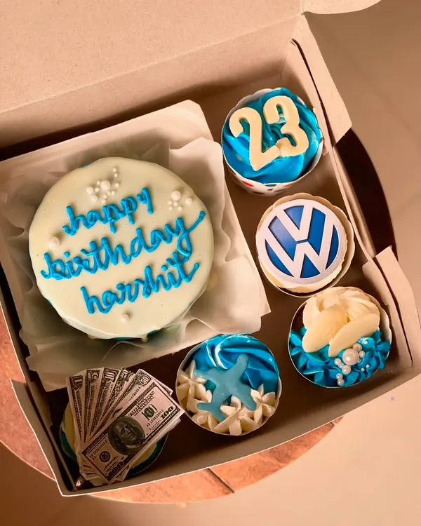This custom bento and cupcake combo is a perfect example of a themed birthday set. The light blue cake with "happy birthday" script is paired with four cupcakes, each decorated with unique toppers like the Volkswagen logo, a number 23, and beach-themed elements, showing how we can personalize a gift for any interest.