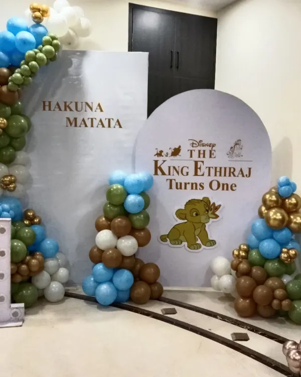 A fun Lion King "Hakuna Matata" theme for a first birthday. I used a custom-printed backdrop with Simba and a balloon arch in earthy tones of green, brown, and blue, plus a light-up number '1'.