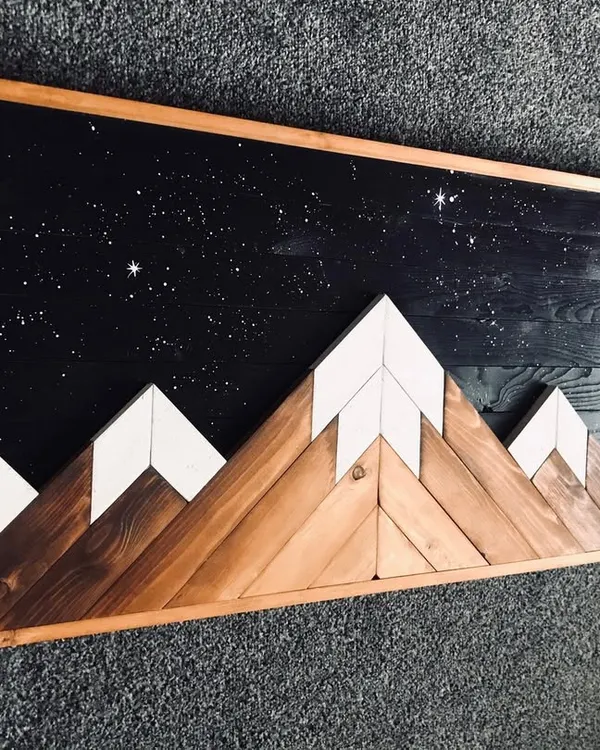 This rustic wooden wall art captures a mountain range against a starry night sky. The contrast between the natural wood grain of the mountains and the dark, speckled sky is stunning.