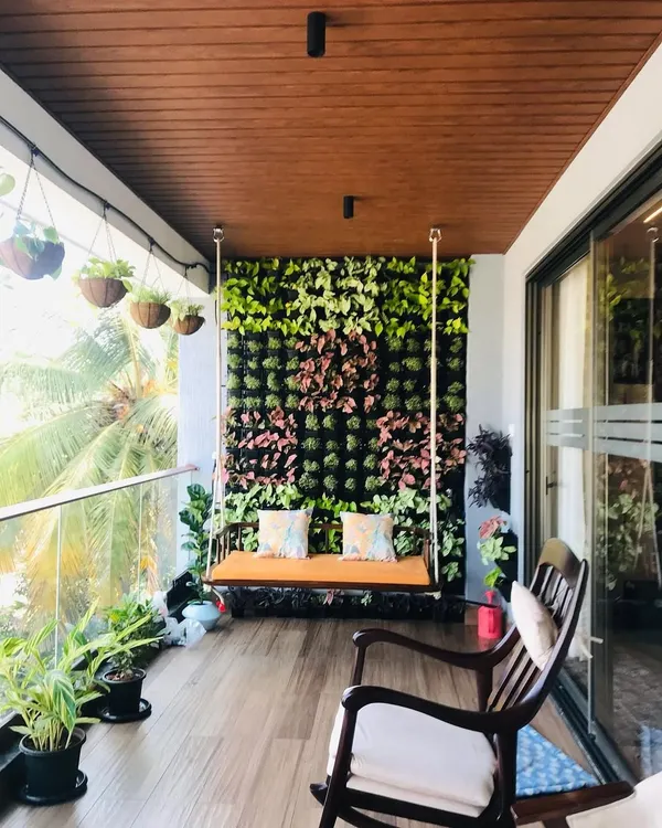 The final result of a balcony transformation. We installed a full-height vertical garden as a stunning backdrop for a wooden swing, complemented by potted plants and hanging baskets to create a lush, private oasis.
