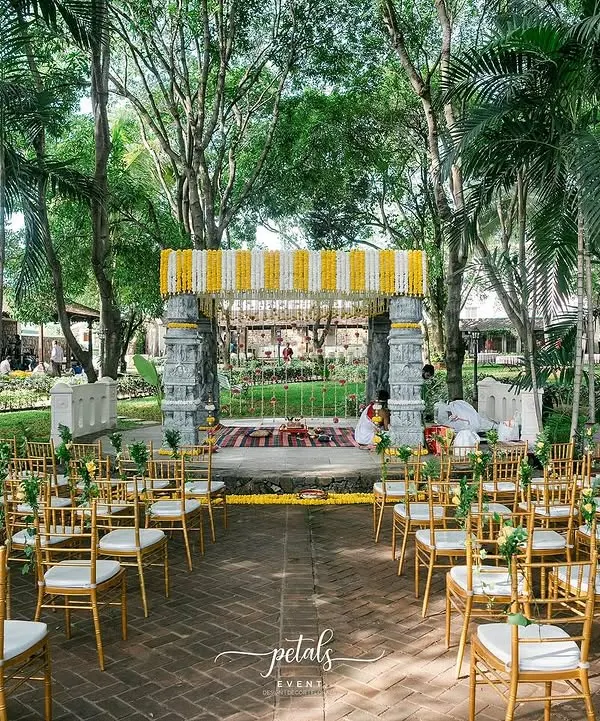 This temple-themed wedding at Angana the Courtyard is a perfect example of how I blend tradition with the beauty of nature. The mandap, framed by ancient trees and adorned with vibrant marigold and chrysanthemum garlands, creates a sacred and breathtaking atmosphere for the ceremony.