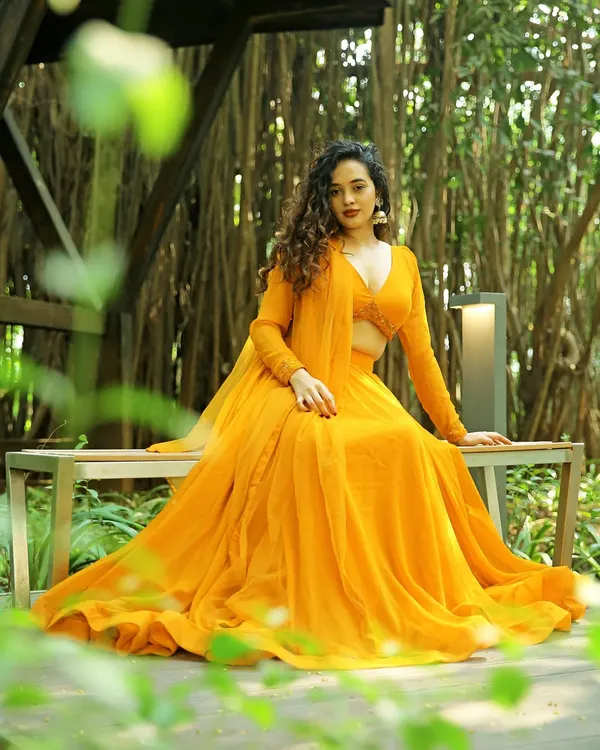 This seated portrait from an outdoor ethnic wear shoot shows how a different pose can highlight the garment's drape and color. The lush background frames the model, making the bright yellow lehenga the center of attention.
