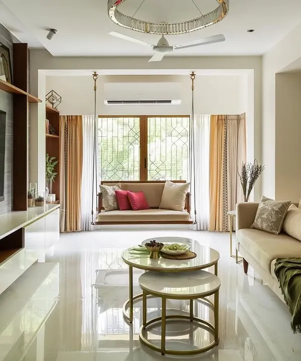 The living room of the Calm Abode, featuring a comfortable beige sofa, nested marble coffee tables, and a traditional wooden swing. The space is bathed in natural light, creating a warm and inviting atmosphere.