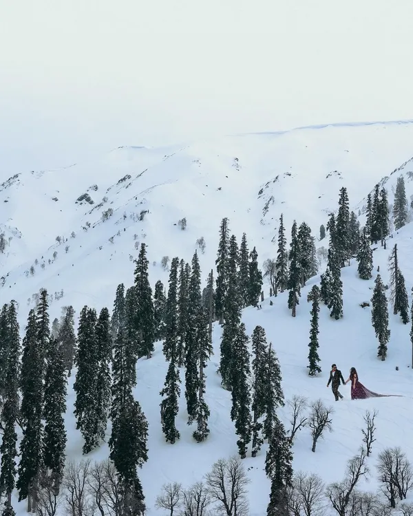 A breathtaking wide shot of a couple walking through the snow-covered landscapes of Kashmir. This is the kind of epic, cinematic pre-wedding photography we love to create.
