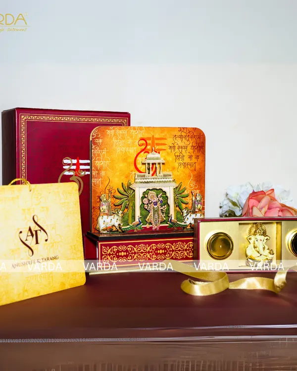 This invitation suite is themed around Shreenathji, featuring temple-style artwork on the box and cards. The set includes a 3D devotional box, a gift bag, and a smaller hamper with a Ganesha idol, creating a complete spiritual gifting experience.