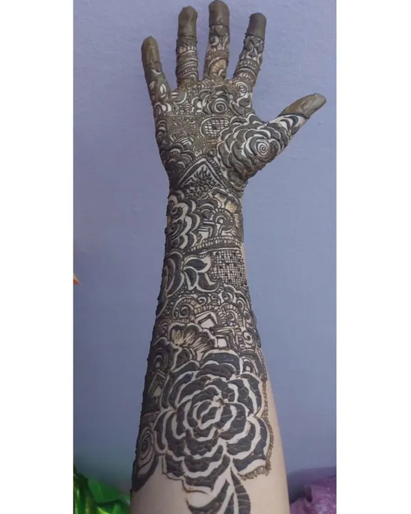 This is a full-arm design with fresh henna paste, showing the right hand. The pattern is dense with large rose motifs and traditional Indian filler patterns.