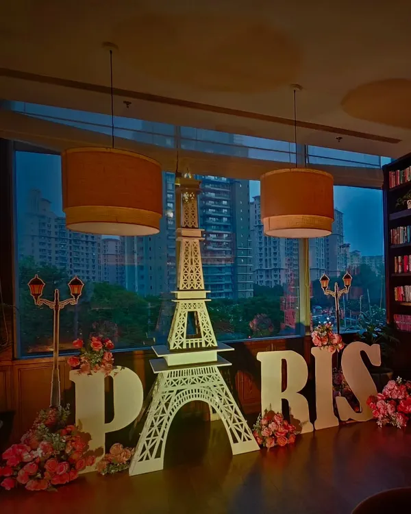A stunning Paris themed setup against the city skyline. This decor for a corporate event included a large Eiffel Tower replica, "PARIS" marquee letters, and romantic floral details.