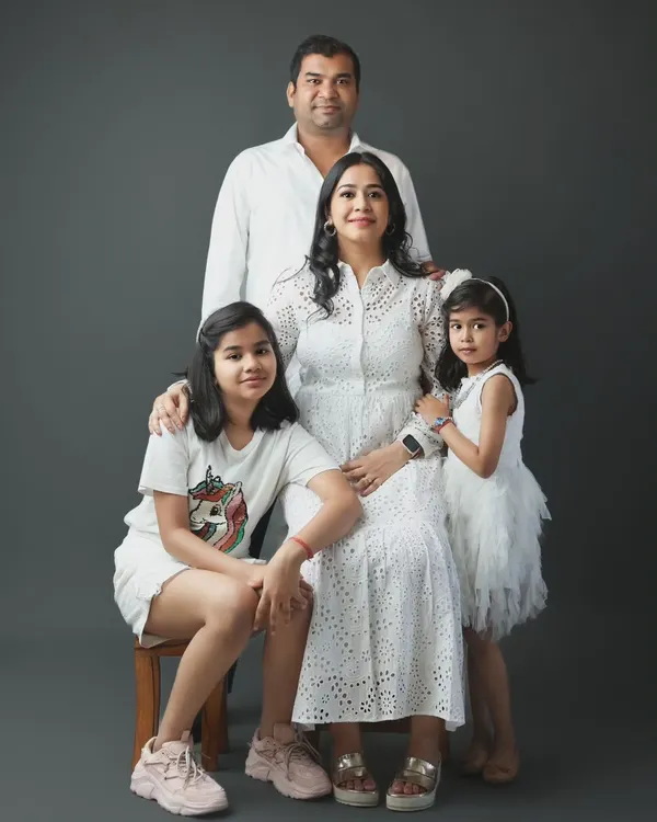 This is a classic family portrait from our Noida studio. We arranged this family of four, with parents and two daughters, for a timeless look against a simple grey backdrop, highlighting their connection and coordinated white outfits.