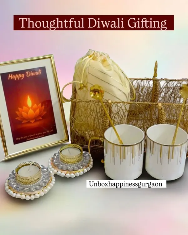 The 'Golden Glow' Diwali basket, featuring two elegant white and gold mugs, matching spoons, decorative pearl diyas, and a 'Happy Diwali' photo frame. This hamper is perfect for couples.