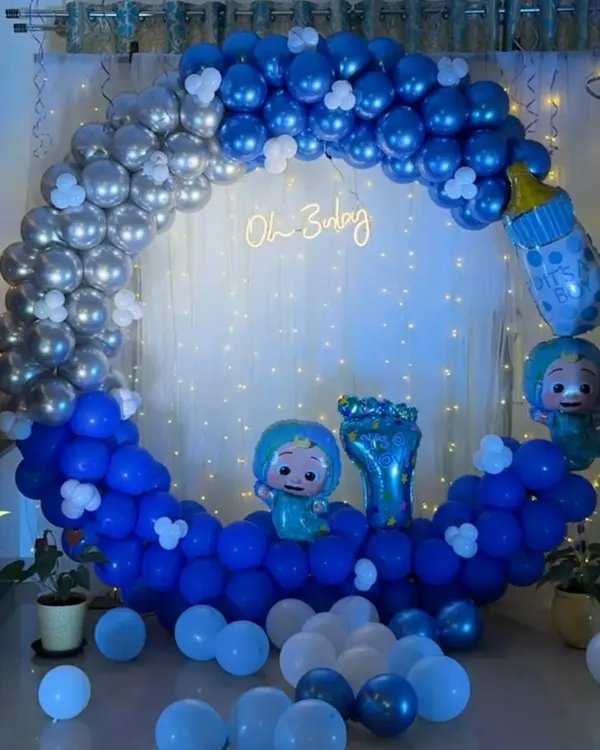 This is a complete 'Oh Baby' themed setup I created for a baby shower in Bangalore. It features a circular backdrop with a blue and silver balloon arch, a custom 'Oh Baby' neon sign, Cocomelon character foil balloons, and a curtain of fairy lights for a magical effect.