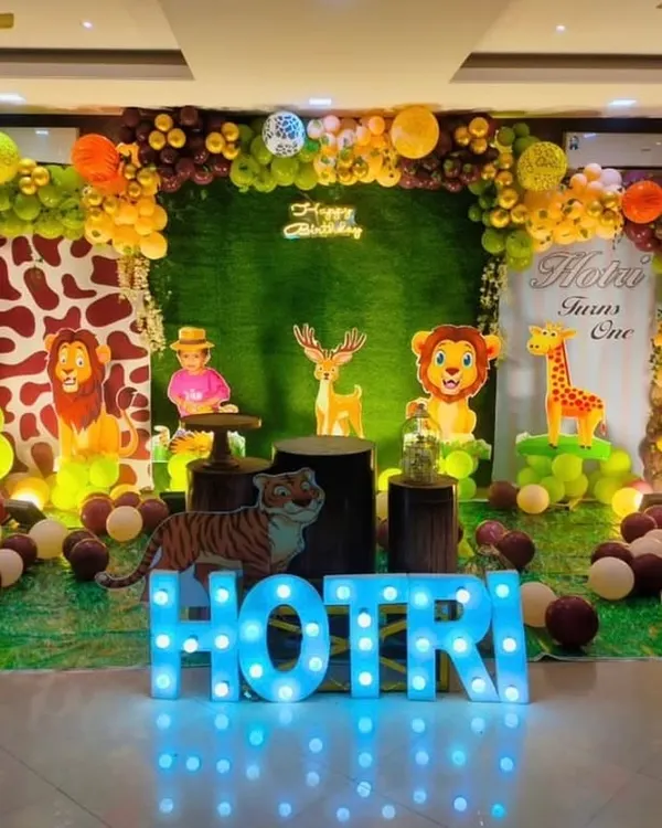 A grand safari-themed first birthday party setup. This decoration features a hedge wall, animal cutouts, a custom welcome sign, marquee letters, and an organic balloon arch in jungle-inspired colors.