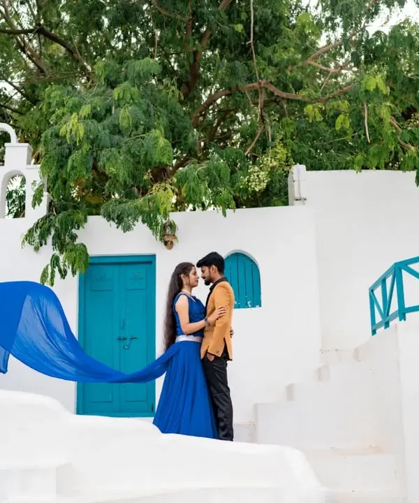 A picture-perfect moment with a Santorini vibe. The bride's flowing blue gown creates a stunning wave of color against the white architecture and blue doors.