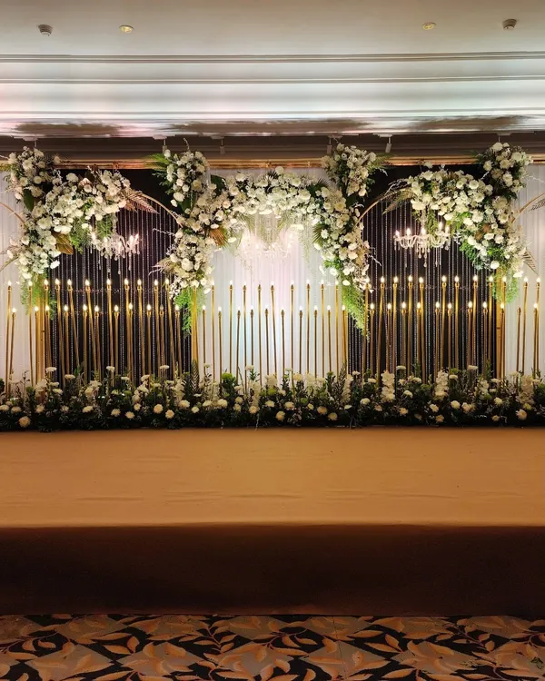 A full view of our candle wall stage design, where hundreds of lights create a warm, mesmerizing glow. This setup, framed by arches of white flowers, is perfect for a grand wedding reception or an elegant awards night.