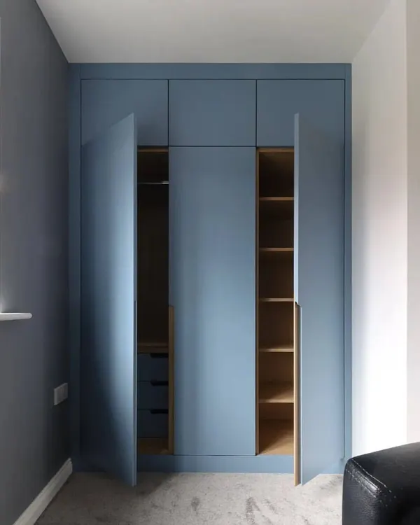 This floor-to-ceiling wardrobe in a matte blue finish features sleek, long handles and offers immense storage. The doors are open to reveal the custom interior with both hanging space and shelving.