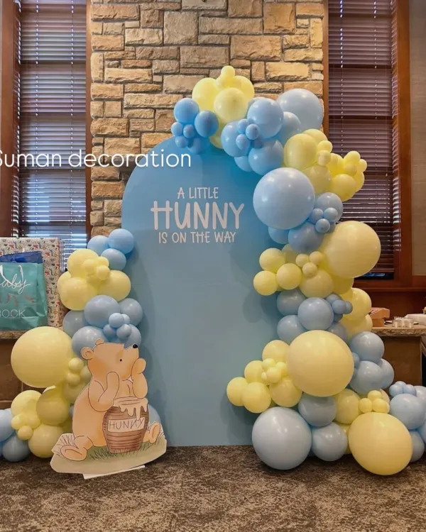 A sweet Winnie the Pooh themed baby shower. The backdrop reads "A Little Hunny is on the way" and is framed by a beautiful balloon garland in pastel yellow and blue.
