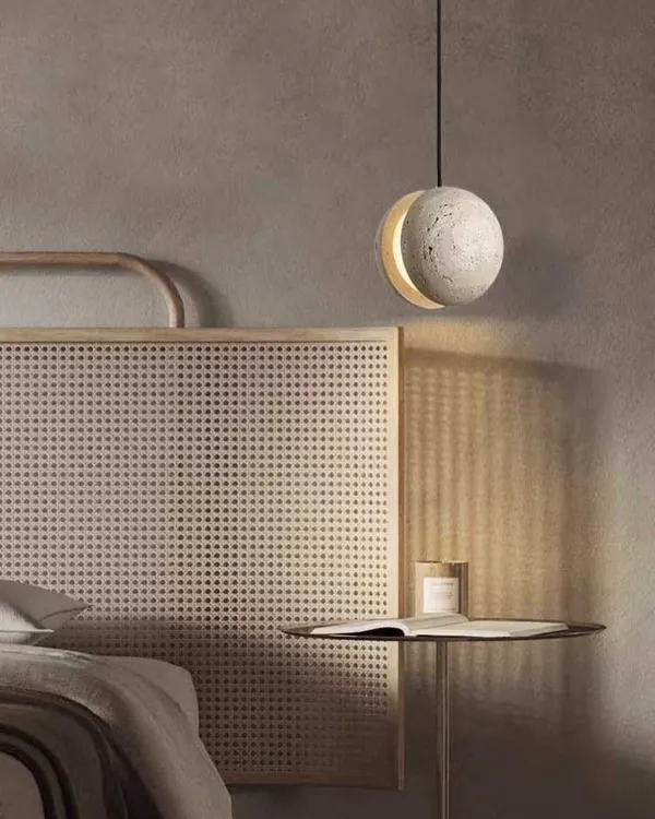 A beautiful pendant light made from natural stone, hanging as a bedside lamp. The light gives the stone a warm, moon-like glow, perfect for a serene bedroom.