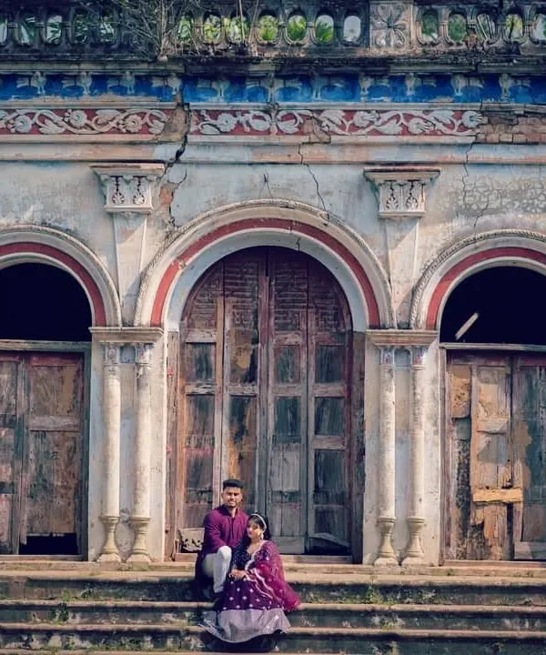 A couple dressed in traditional attire posing in front of a beautiful old haveli, giving the photo a royal and historic feel.